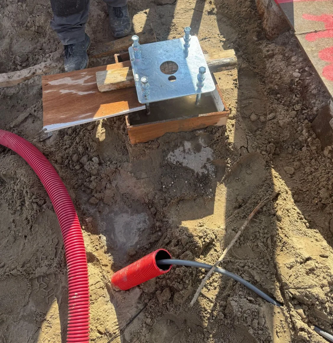 Grondanker in vers beton, met een grijze netwerkkabel die uit een rode flexbuis komt
