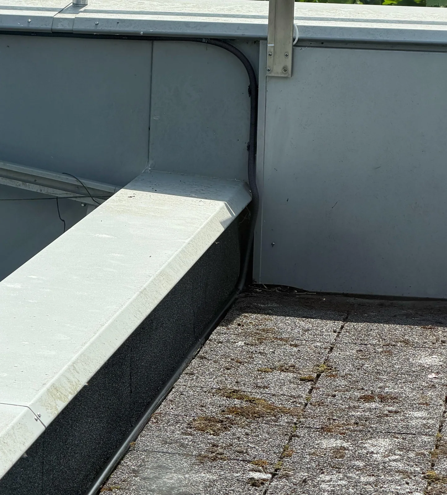 Zwarte kabelbuis langs de opstand van een plat dak, zonder door het dak te gaan, bij een woning in Kropswolde