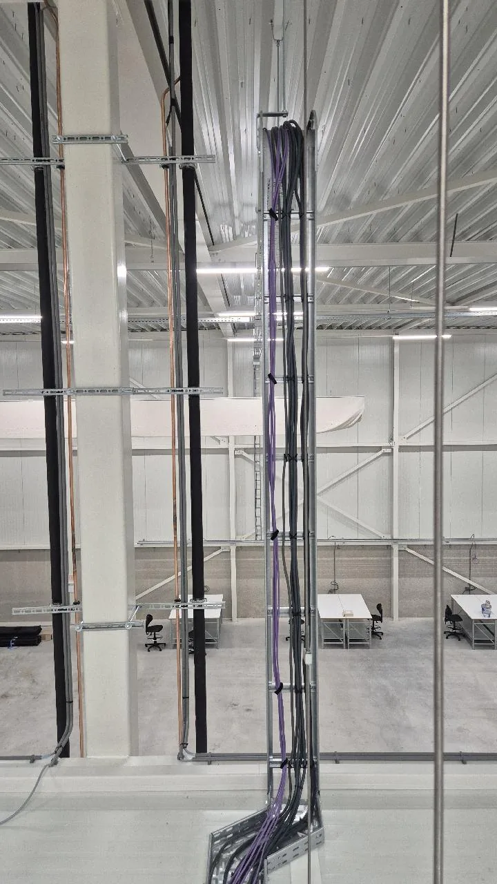 Gebundelde paarse en zwarte kabels die verticaal langs een kolom naar de kabelgoot lopen in een lege warehousehal