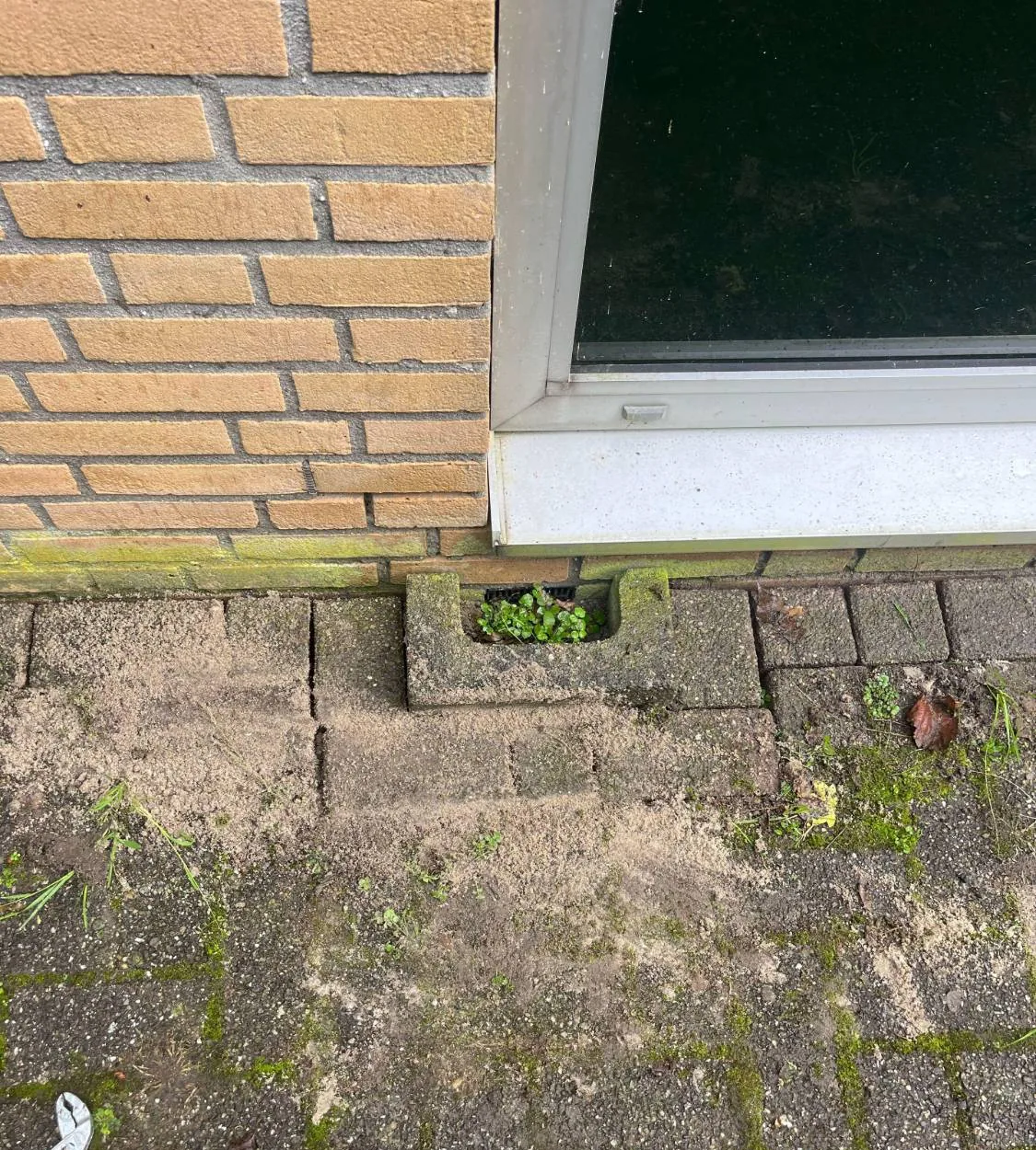 Kabeldoorvoer in een gevel van gele baksteen naast een ventilatierooster onder een raam