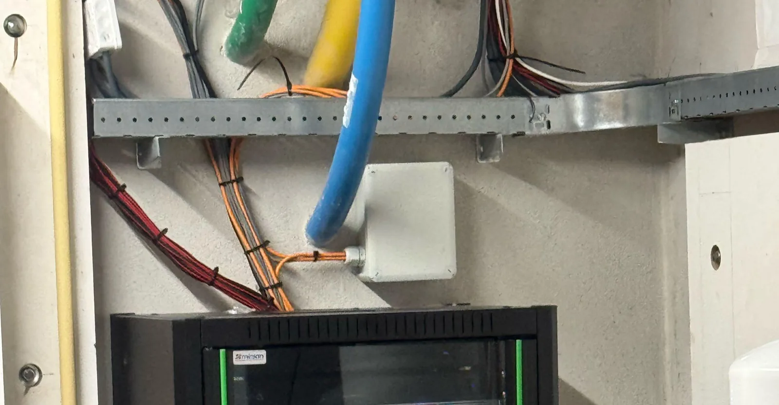 Kabelgoot met gebundelde kabels en een aansluitdoos boven de patchkast in de technische ruimte
