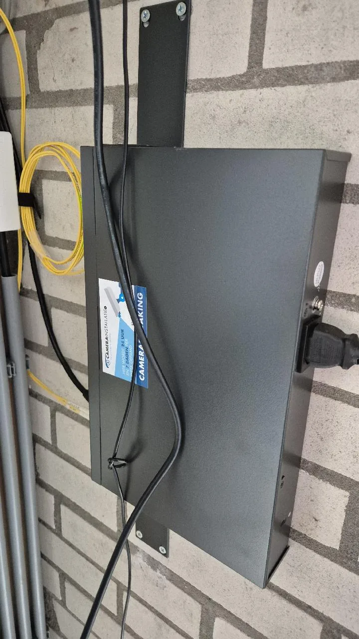 Donkere kast tegen een bakstenen wand in het technische hokje, met de gele glasvezel ernaast