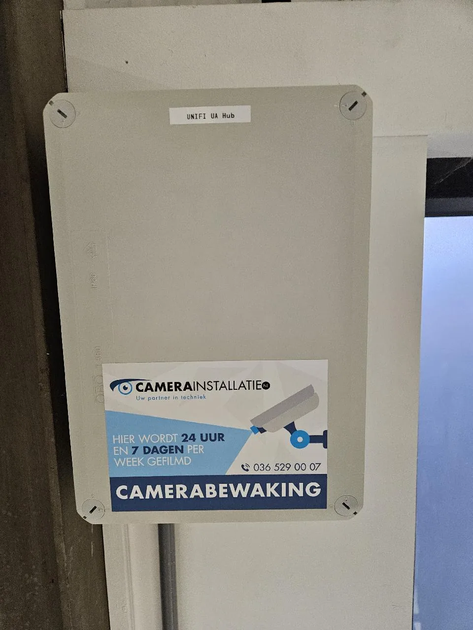 Gesloten kunststof kast met het label UniFi UA Hub, links boven de achterdeur