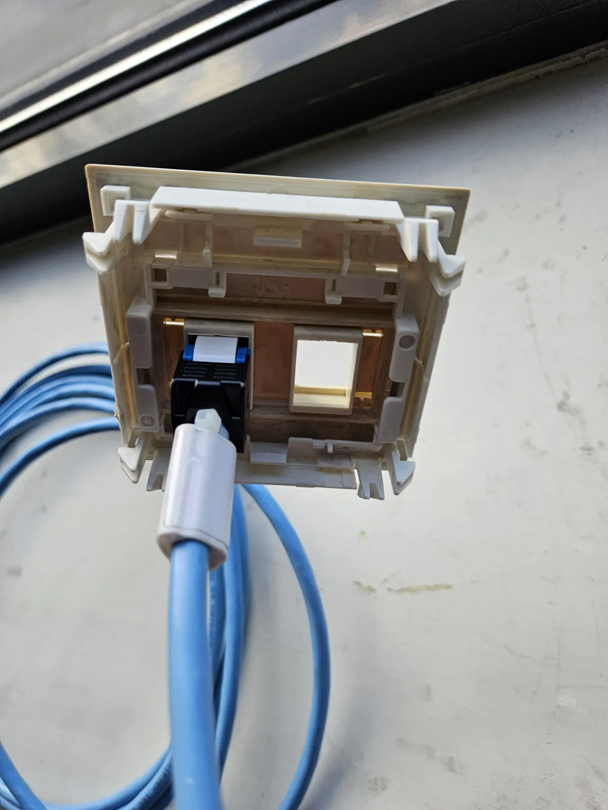 Achterkant van een faceplate met een nieuwe keystone op een lichtblauwe netwerkkabel