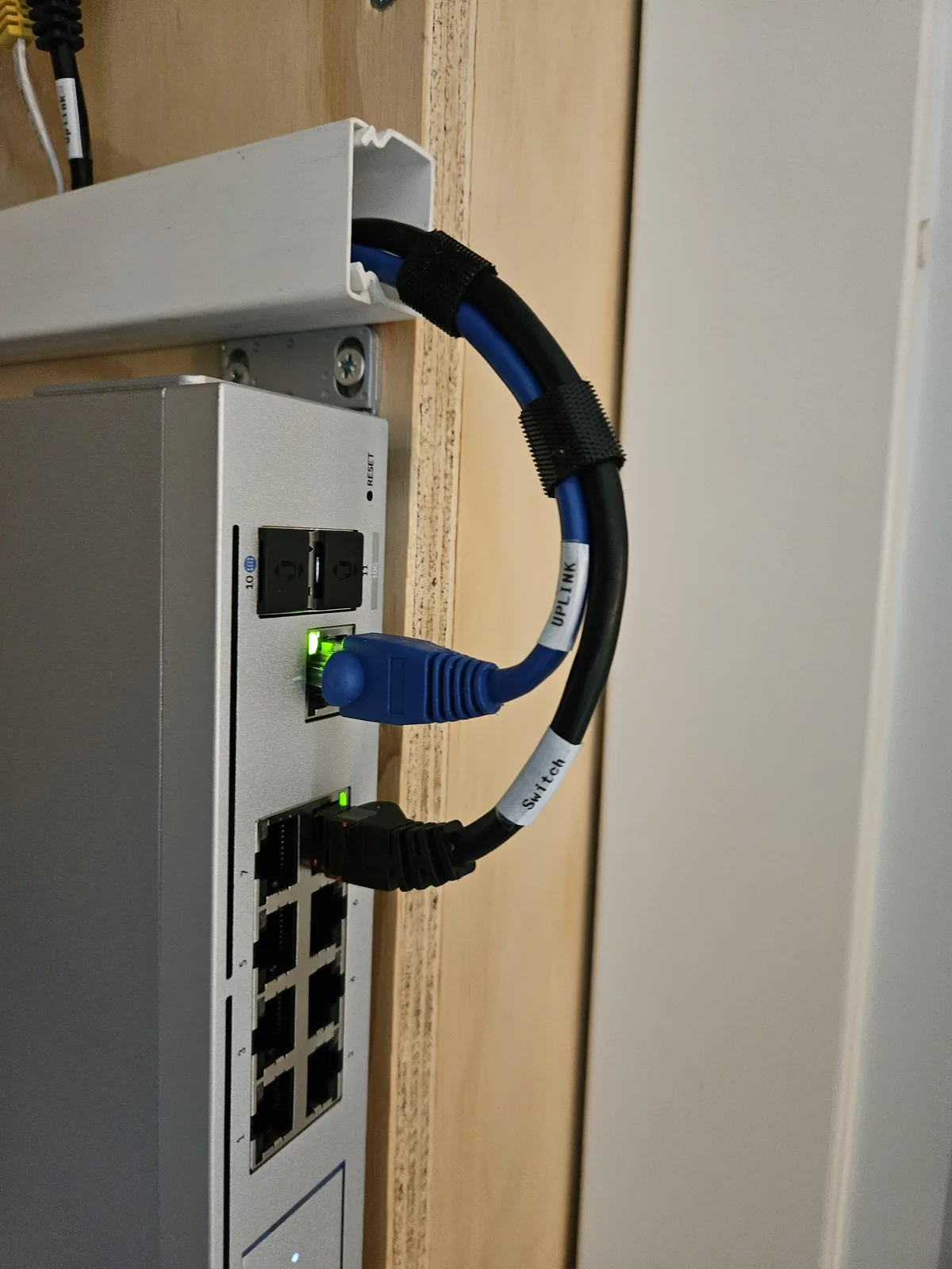 Een blauwe en een zwarte patchkabel met labels Uplink en Switch, met klittenband gebundeld boven op de UniFi Dream Machine