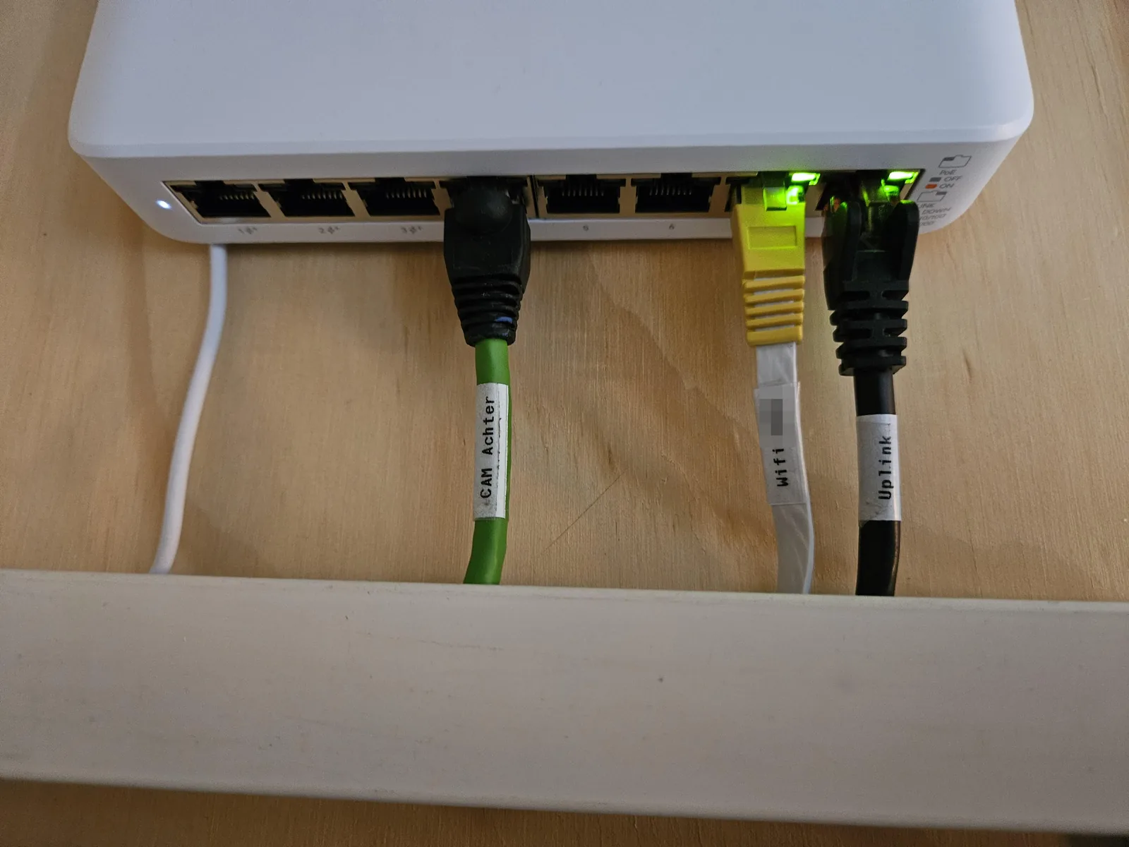 Close-up van de labels CAM achter, wifi en Uplink op de kabels onder de PoE-switch