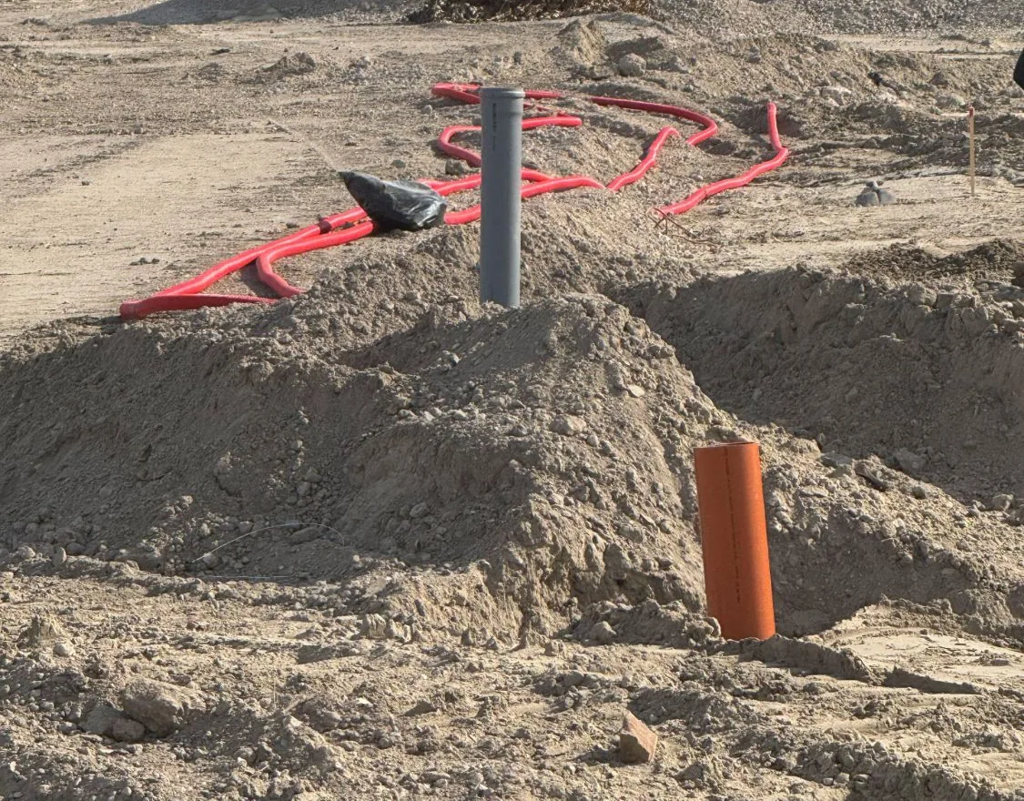 Leeg bouwterrein met rode flexbuizen en mantelbuizen die uit het zand steken