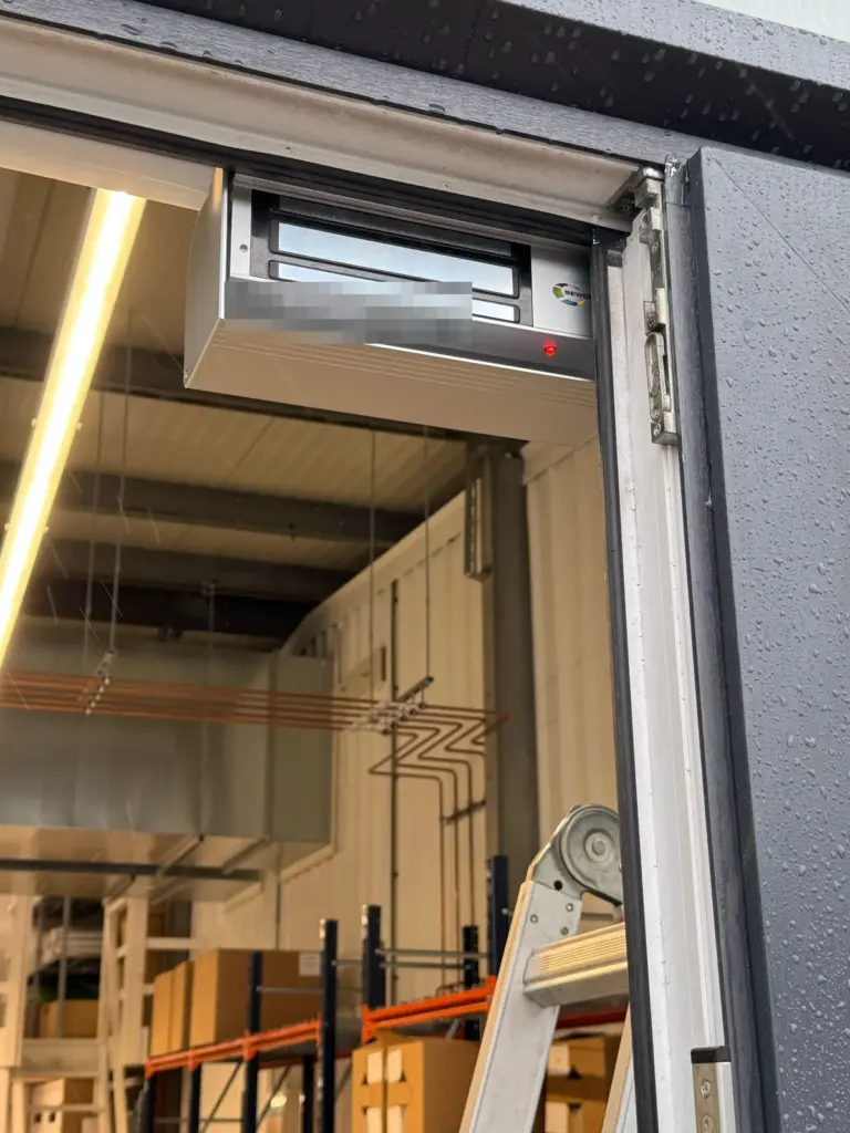 Magneetslot van 550 daN boven in het kozijn van de achterdeur van een bedrijfsunit in Haarlem, met de opslag erachter