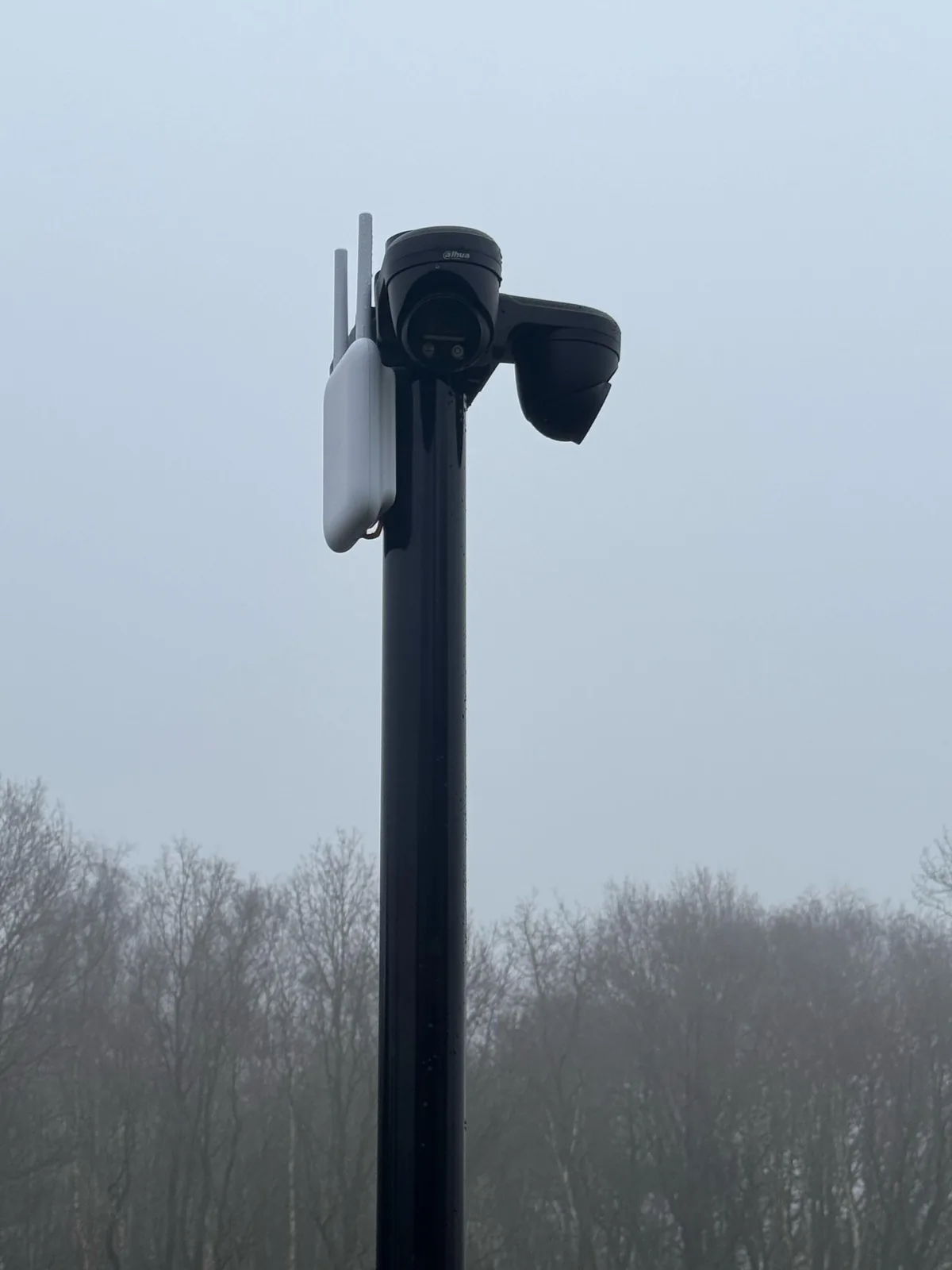 Bovenkant van een zwarte mast met twee Dahua-turrets en een wit UniFi-accesspoint voor buiten