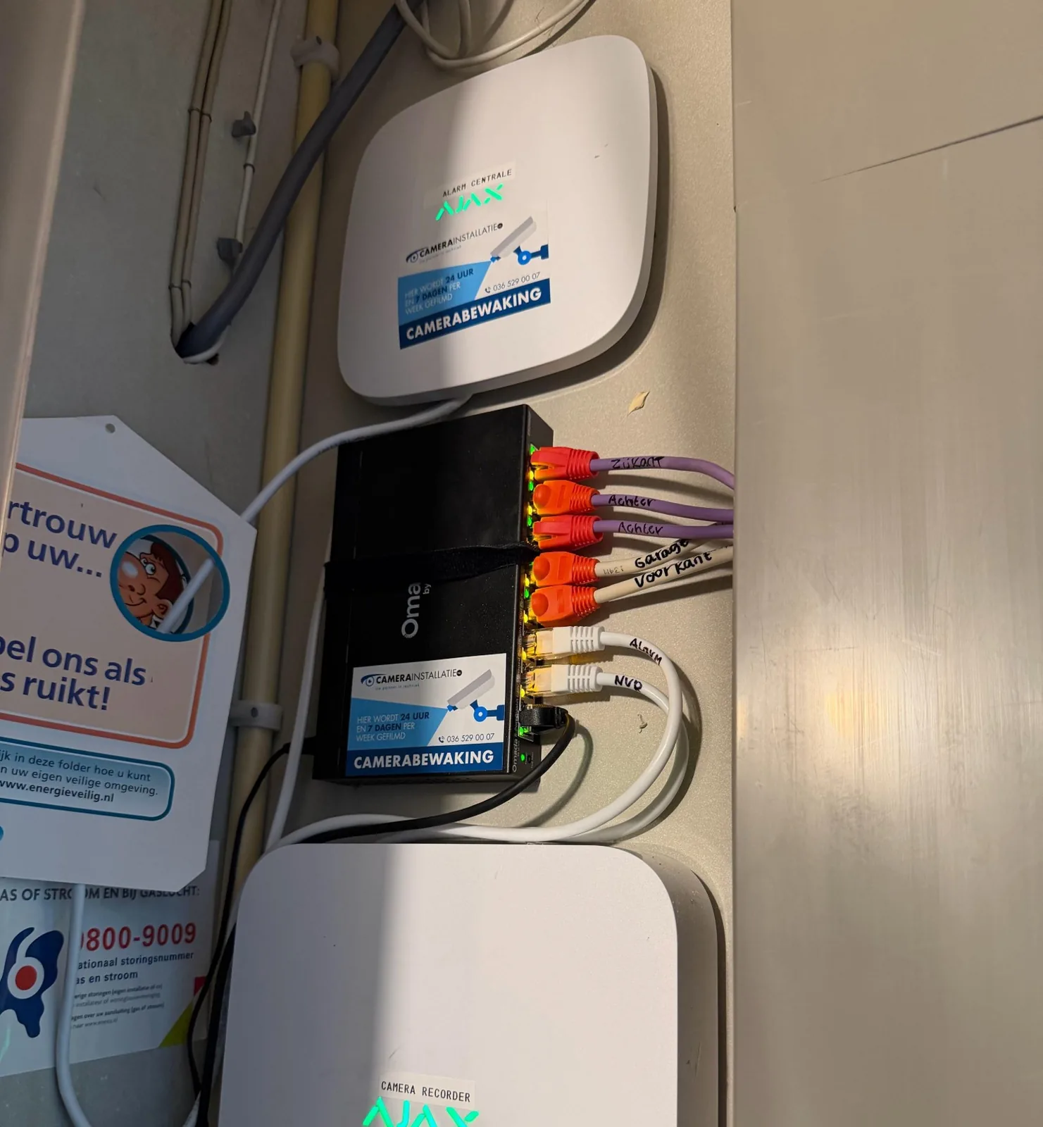 Meterkast met bovenin de witte Ajax-hub van het alarm, daaronder een switch met gelabelde kabels en onderin de Ajax-recorder, bij een woning in Kropswolde
