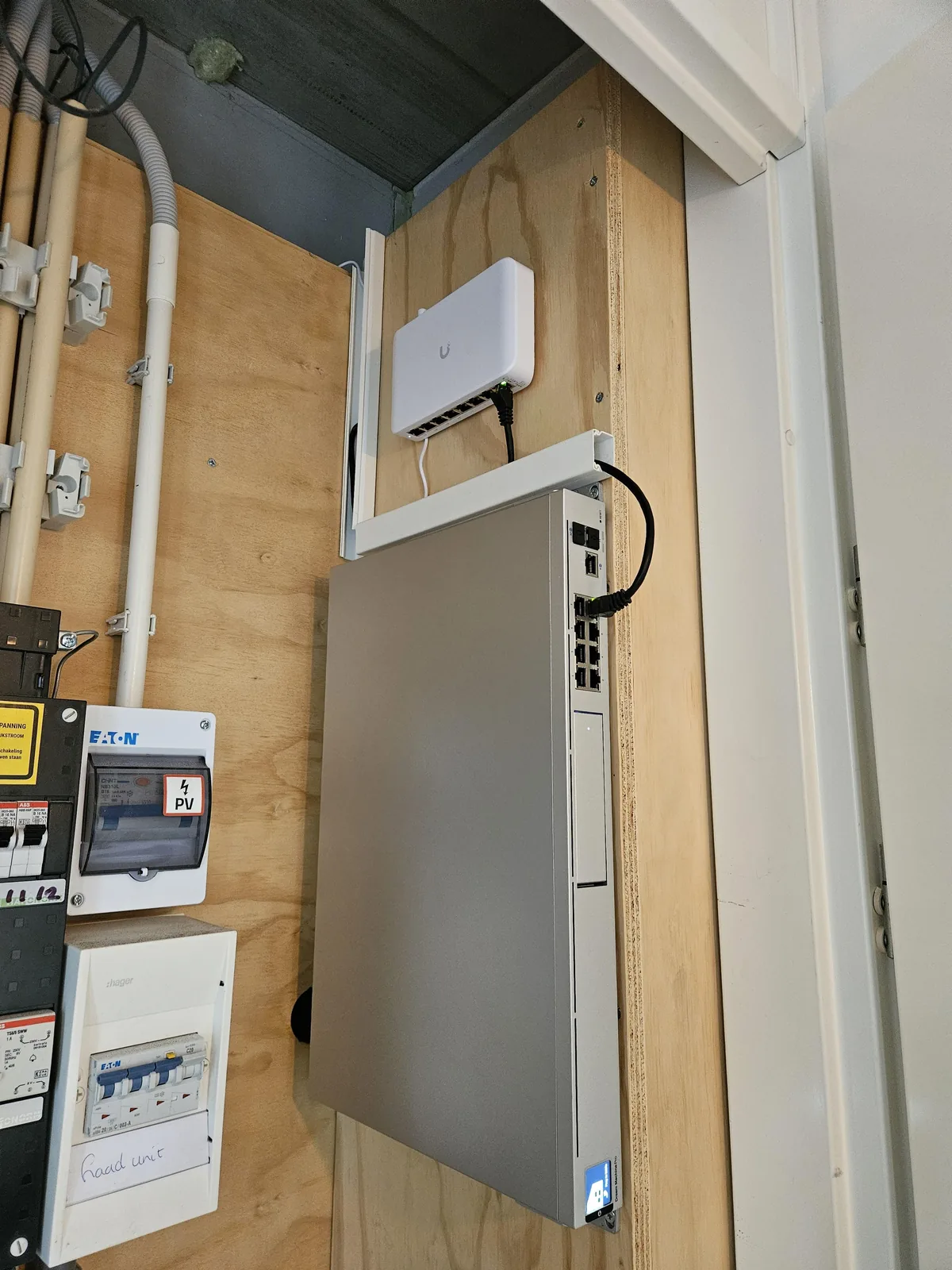 Meterkast met de UniFi Dream Machine en de PoE-switch, de kabels in een wit kabelkanaal ertussen