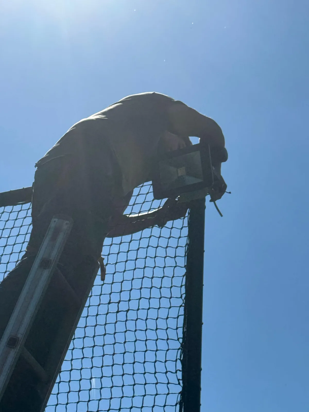 Monteur op een ladder monteert een LED-lamp bovenaan het frame van een ballenvanger