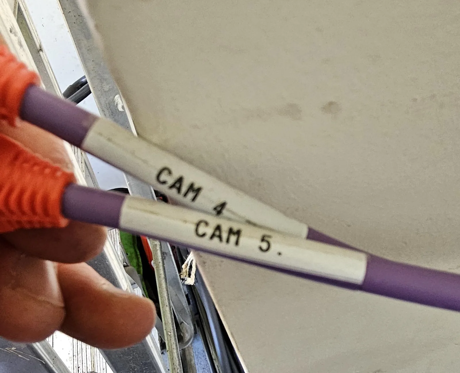 Twee paarse netwerkkabels met witte labels CAM 4 en CAM 5, in een hand met werkhandschoen