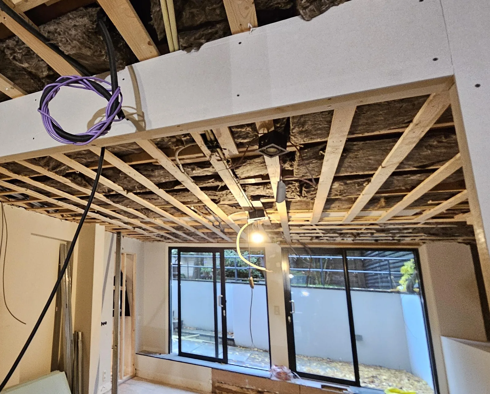 Doorkijk door een open plafond met balken naar de tuinpui, tijdens de verbouwing