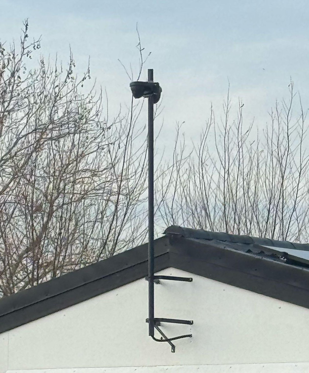 Zwarte paal met camera bovenaan, met twee beugels vastgezet aan de witte topgevel van de schuur