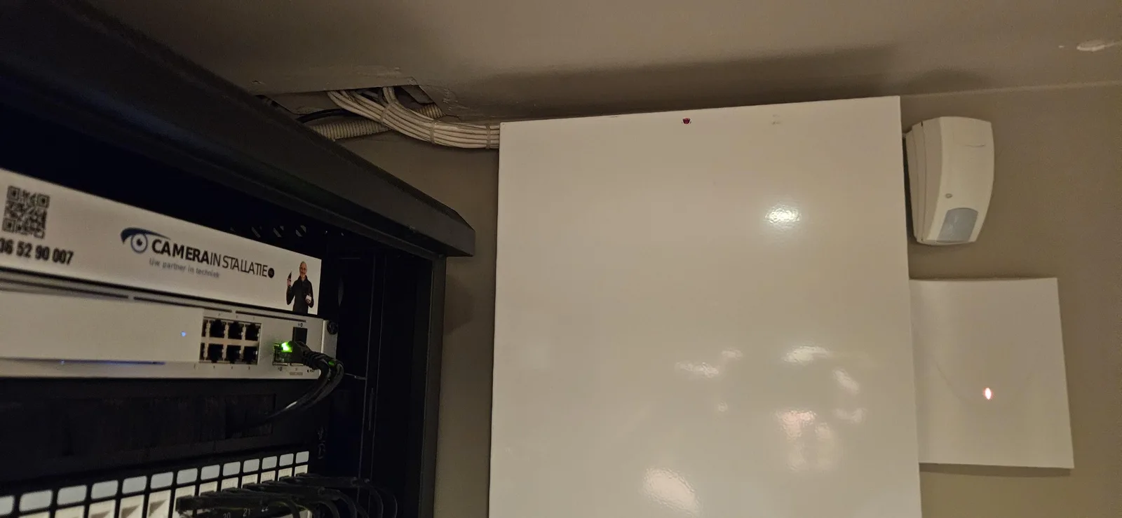 Patchkast met UniFi-apparatuur, met ernaast de kast van de alarmcentrale en een bewegingsmelder