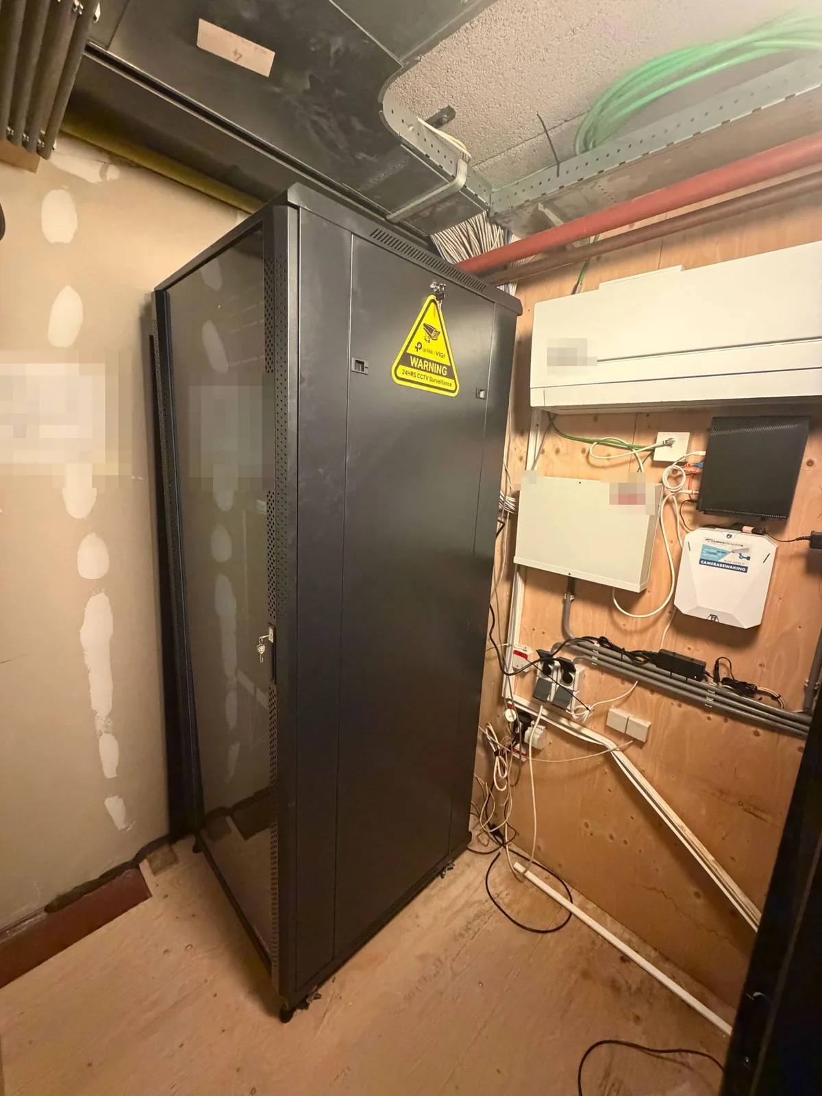 Technische ruimte met een zwarte patchkast en aan de wand de Ajax-hub met de sticker van CameraInstallatie.nl