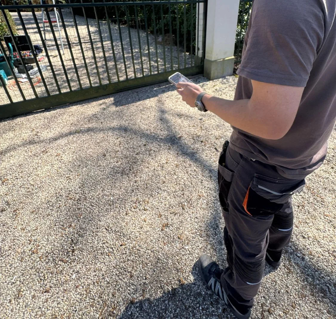 Monteur met een telefoon in de hand voor de schuifpoort op een grindoprit