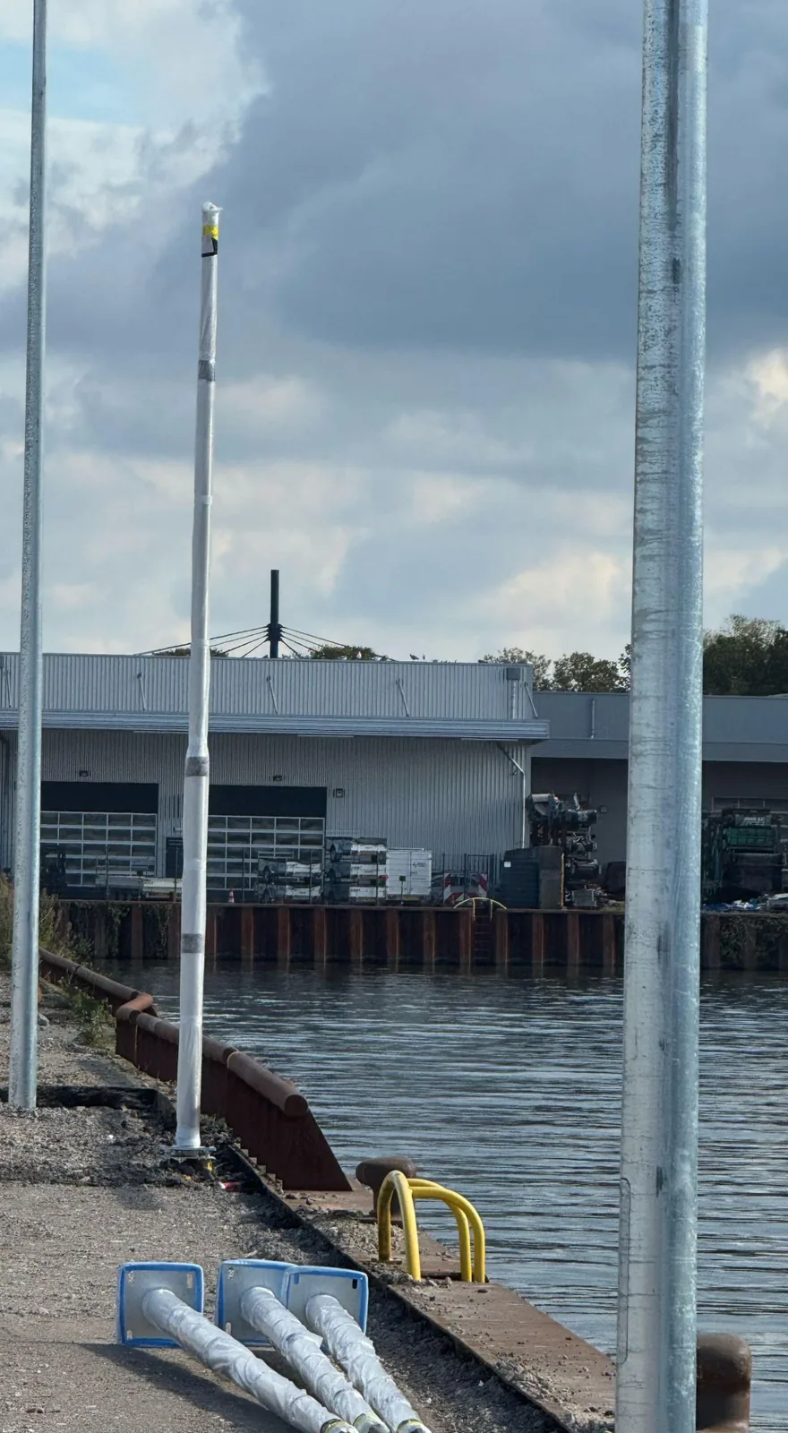 Rij camerapalen langs een kade aan het water, een staand in folie en drie nog liggend met blauwe voetplaten