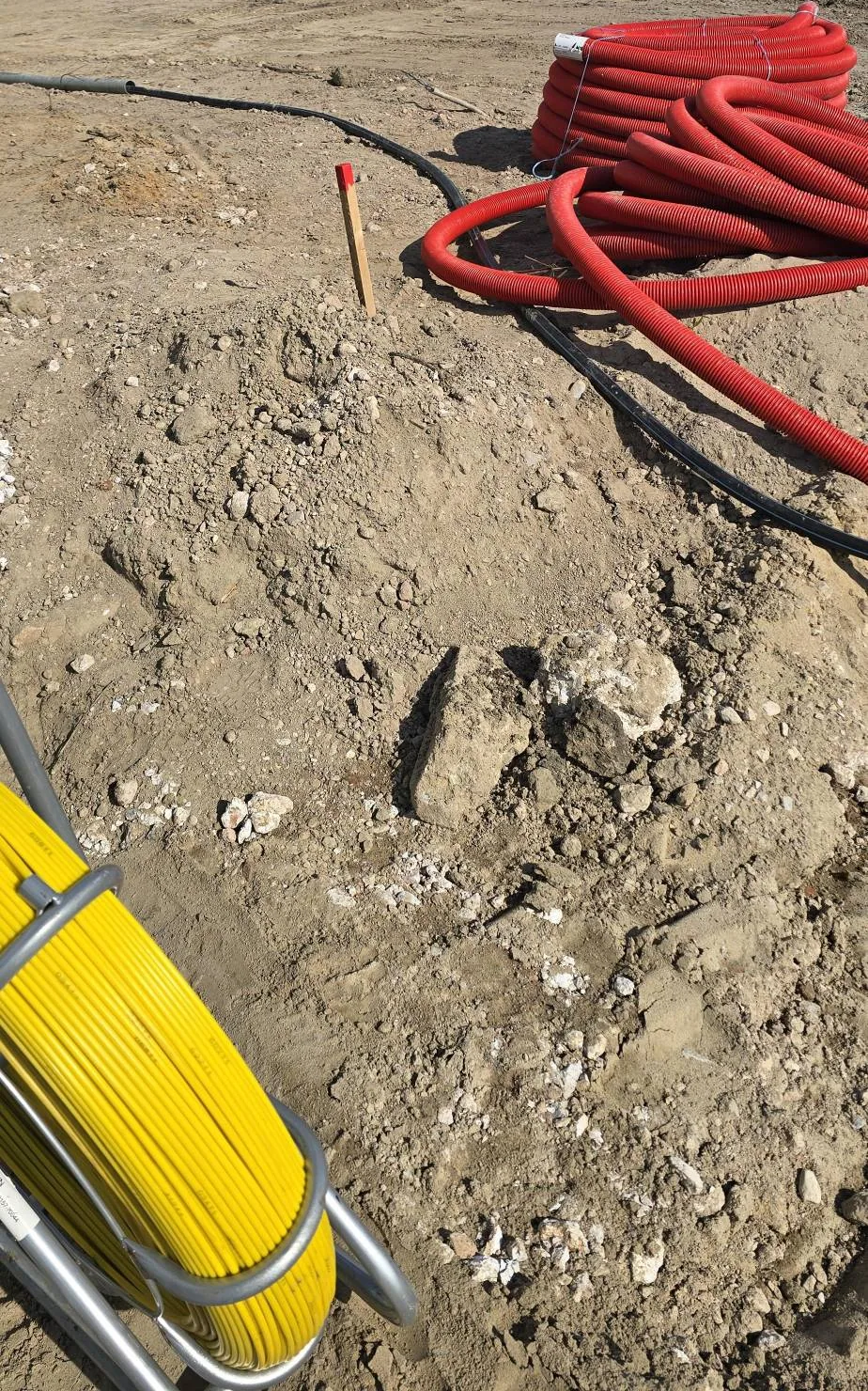 Rollen rode flexbuis en een zwarte mantelbuis op open grond, met een gele kabeltrekveer