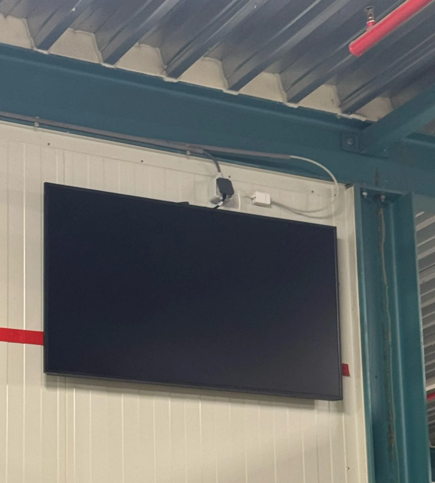 Scherm van 50 inch bij de stalen balk van de hal, met de kabel netjes langs de balk aangevoerd