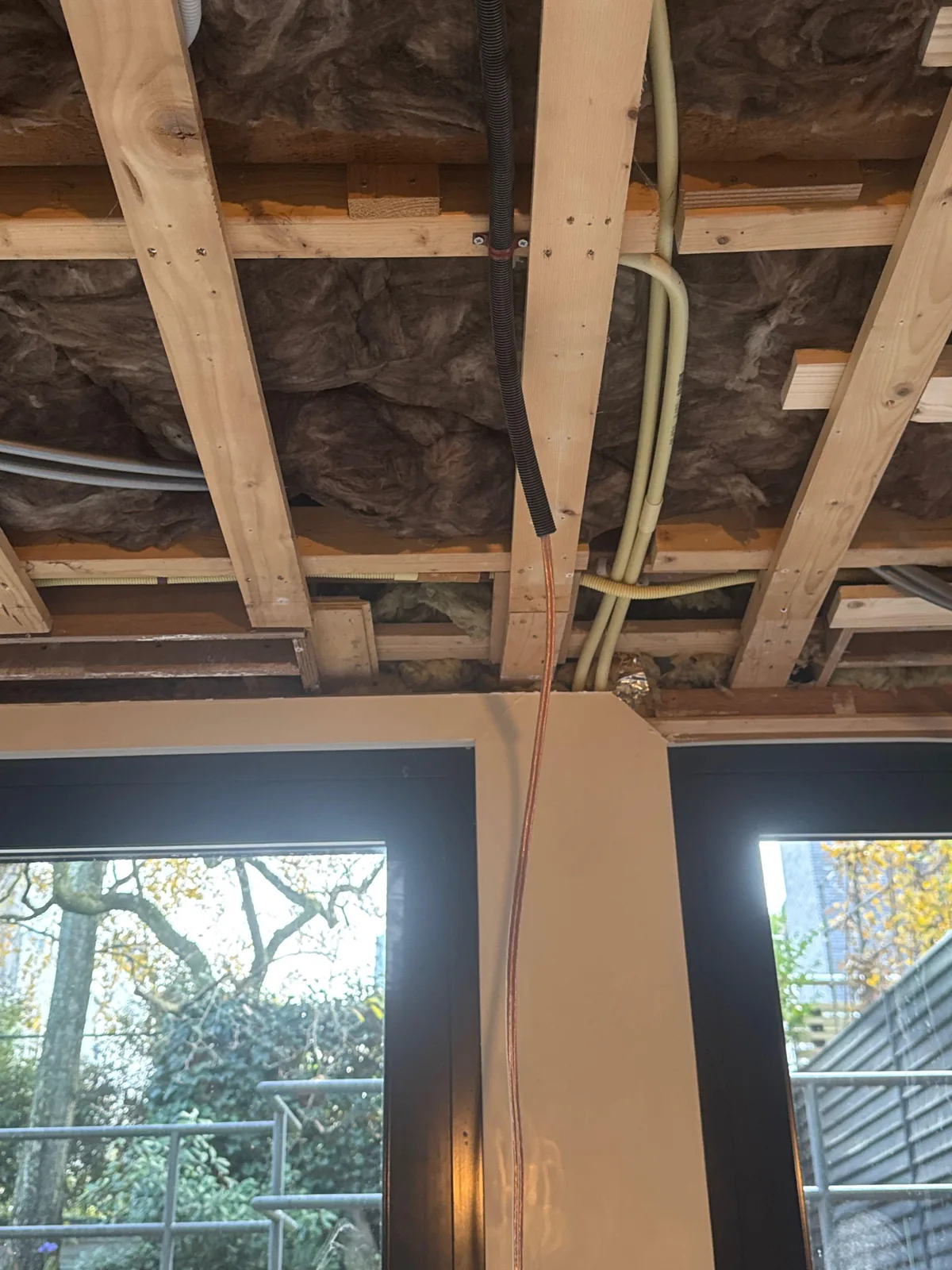 Speakerkabel en flexbuis lopen door een open plafond, vastgezet met klemmen, boven de tuinpui