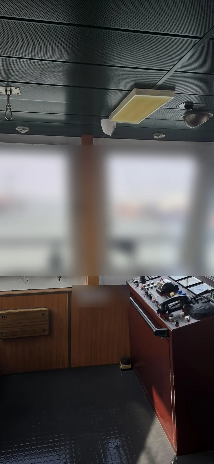 Stuurhut van een containerschip met houten betimmering, een bedieningspaneel en een camera rechts in het plafond