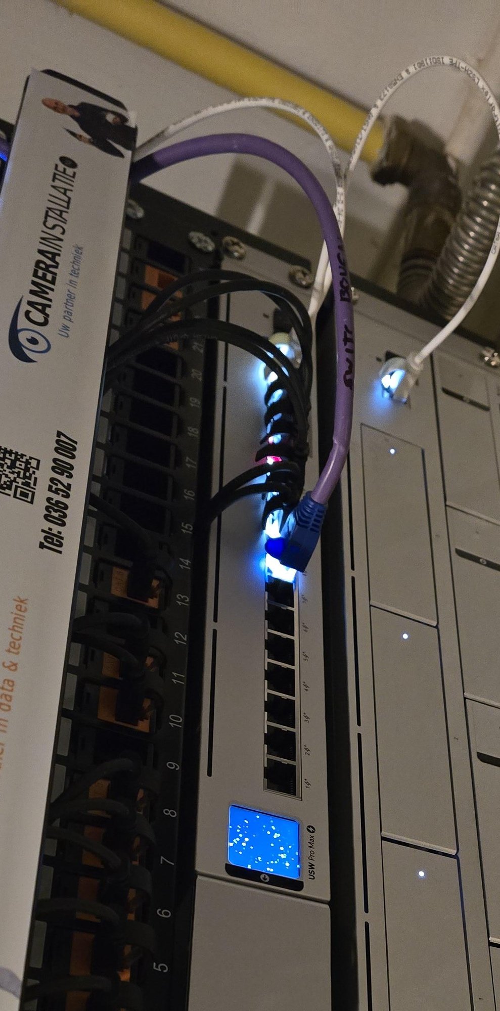Patchpaneel met genummerde poorten en kabels naar de switch, met het logo van CameraInstallatie.nl