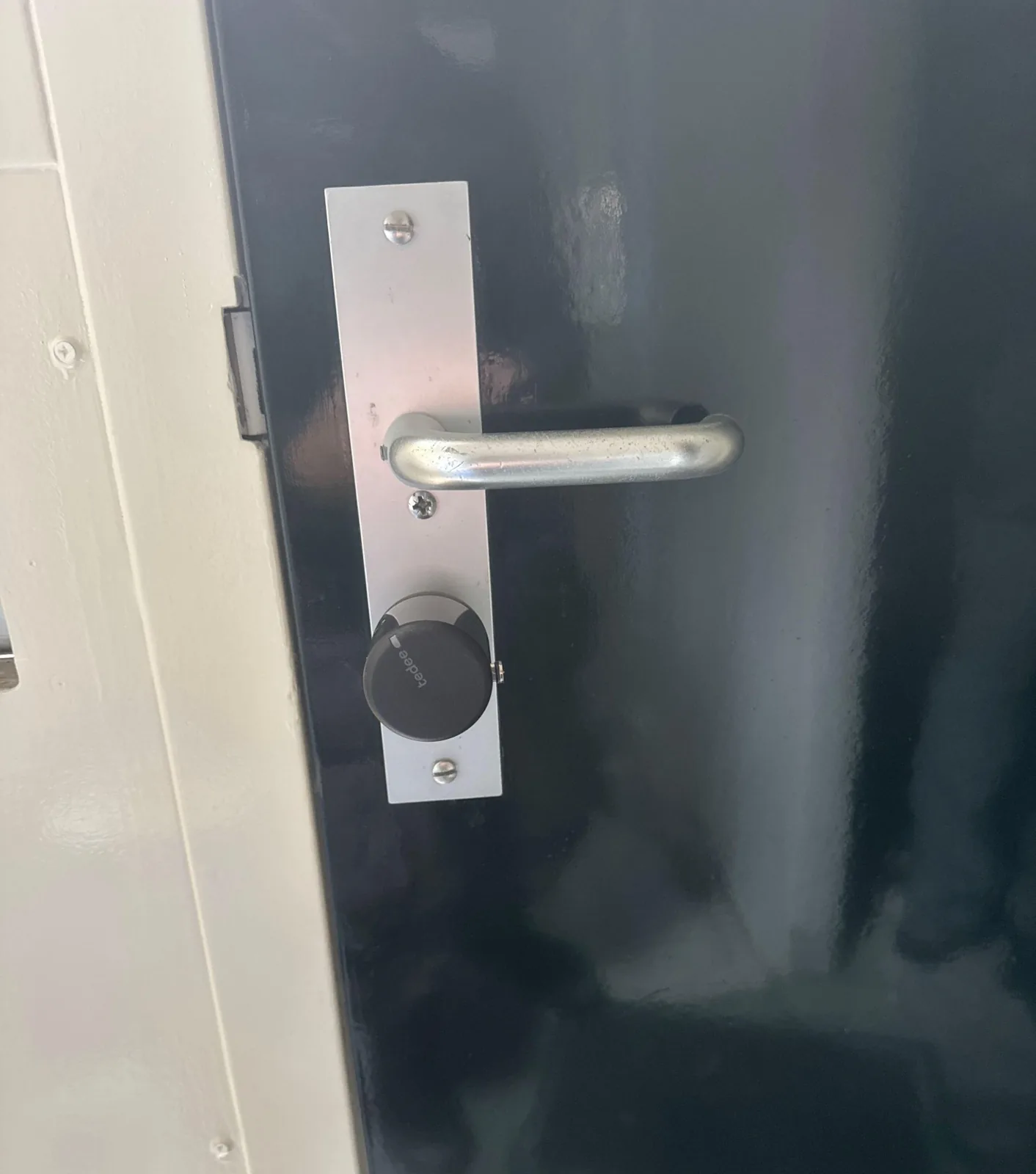 Zwart Tedee slim slot op de cilinder aan de binnenkant van een donkere voordeur, onder de deurklink