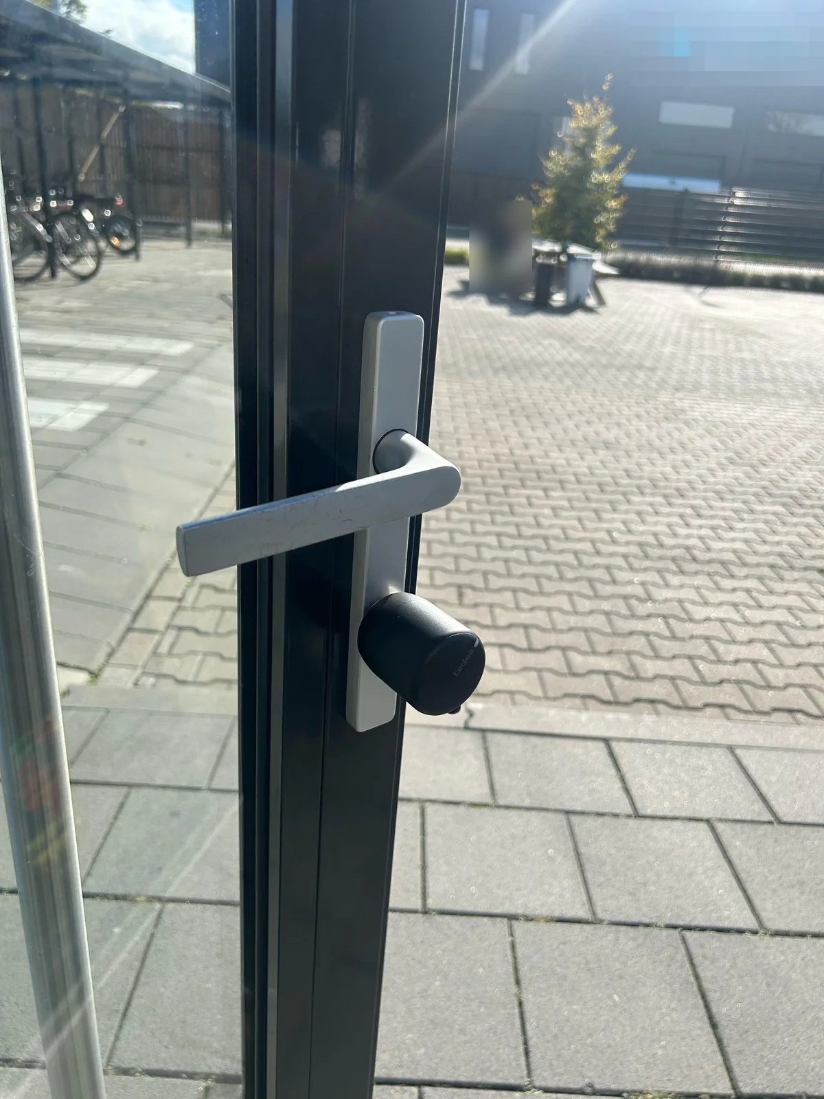 Zwart Tedee slim slot op de cilinder van een aluminium buitendeur van een kantoor, gekoppeld aan een UniFi-intercom