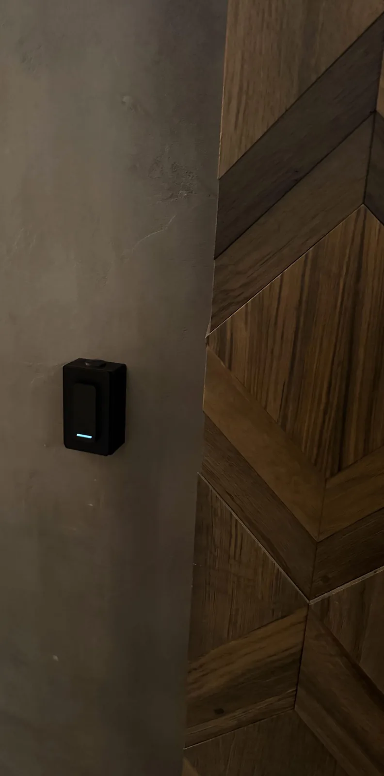 Zwarte toegangslezer op een betonlook-wand, vlak naast houten panelen in een ruitpatroon