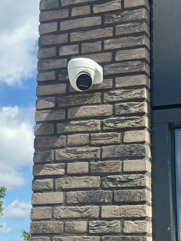 Witte turretcamera op een donkere bakstenen gevel, naast een raam met een zwart kozijn