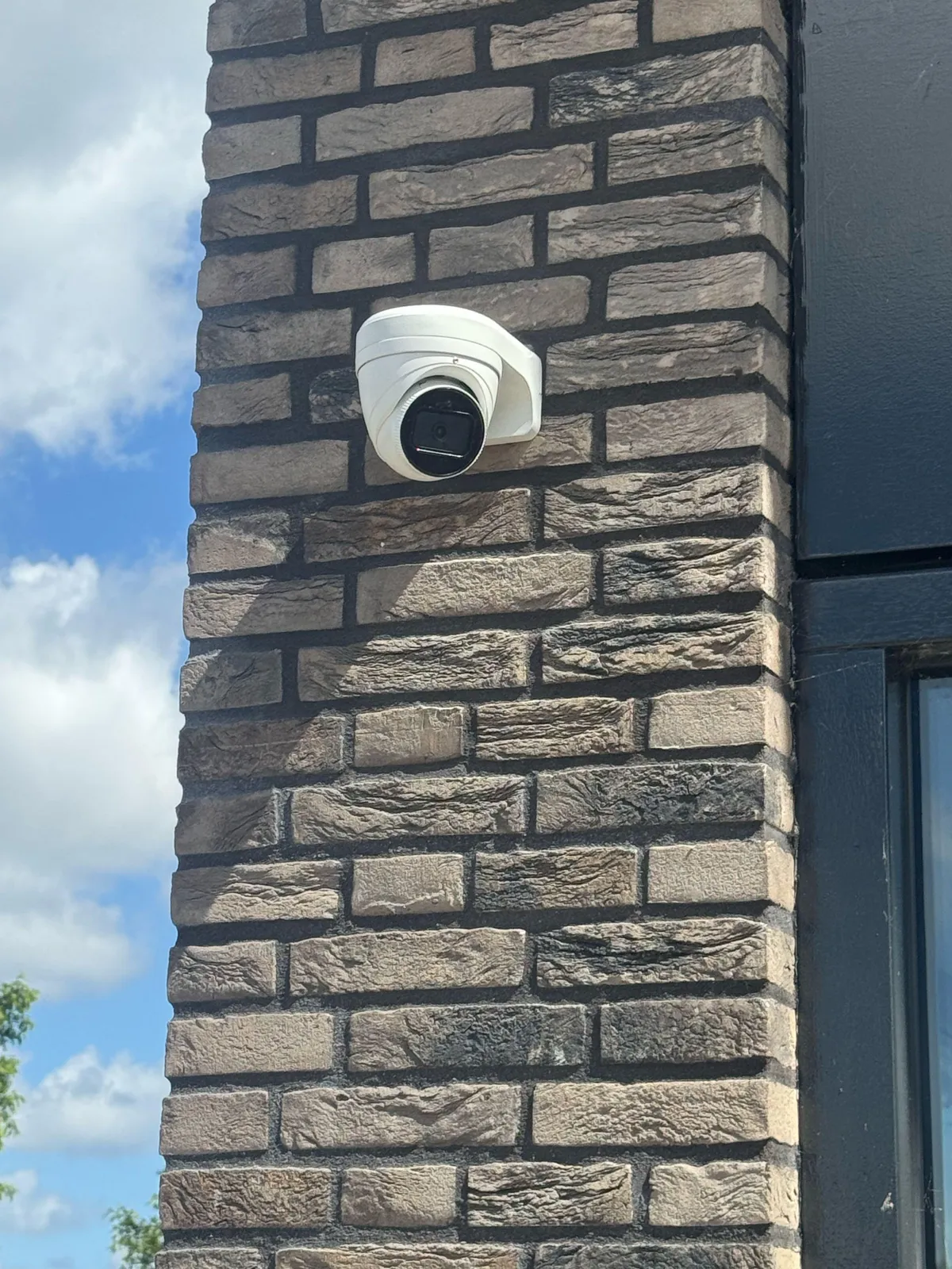 Witte turretcamera op een donkere bakstenen gevel, naast een raam met een zwart kozijn