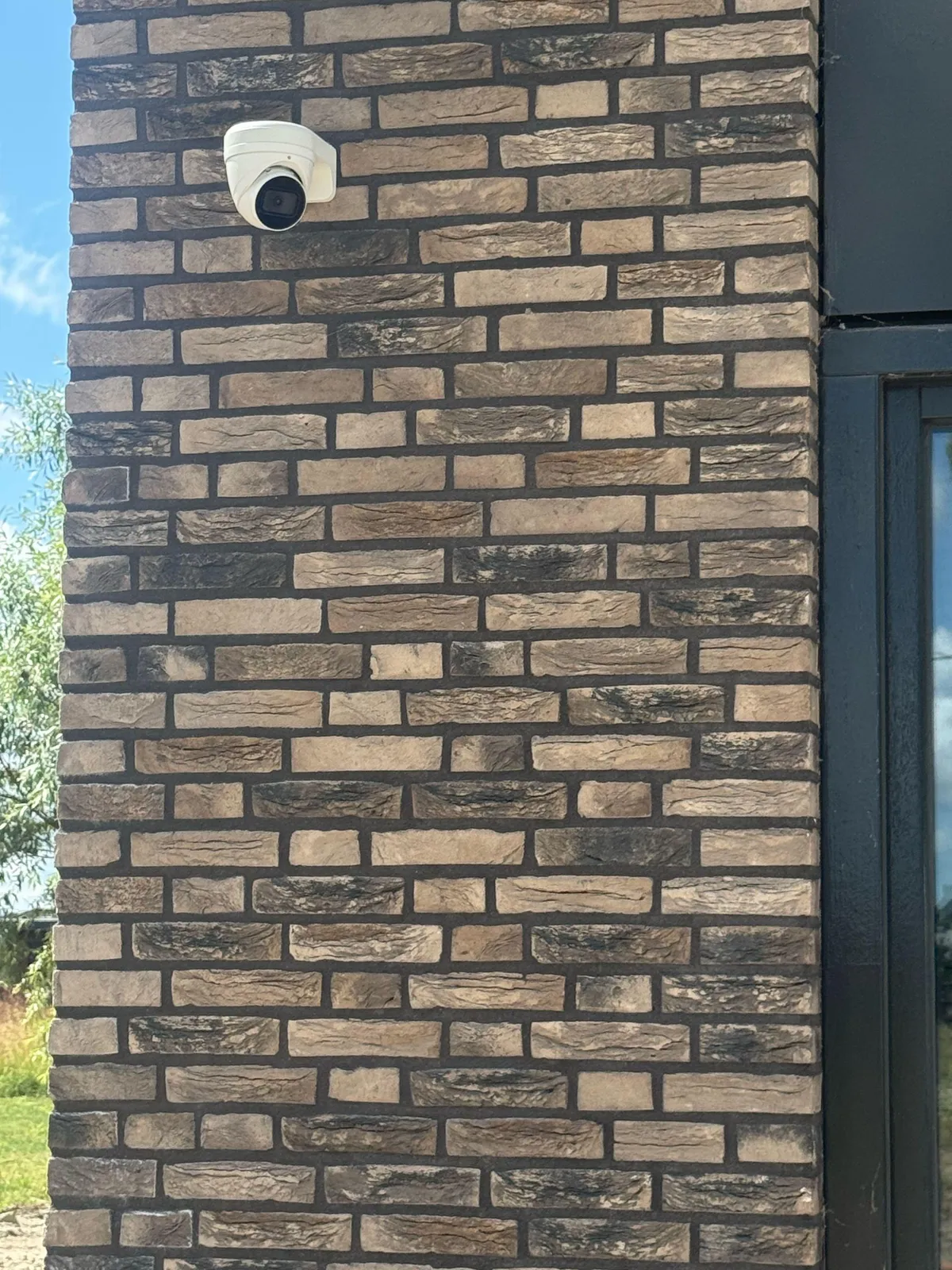 Witte turretcamera hoog op een donkere bakstenen gevel, met lucht en groen op de achtergrond