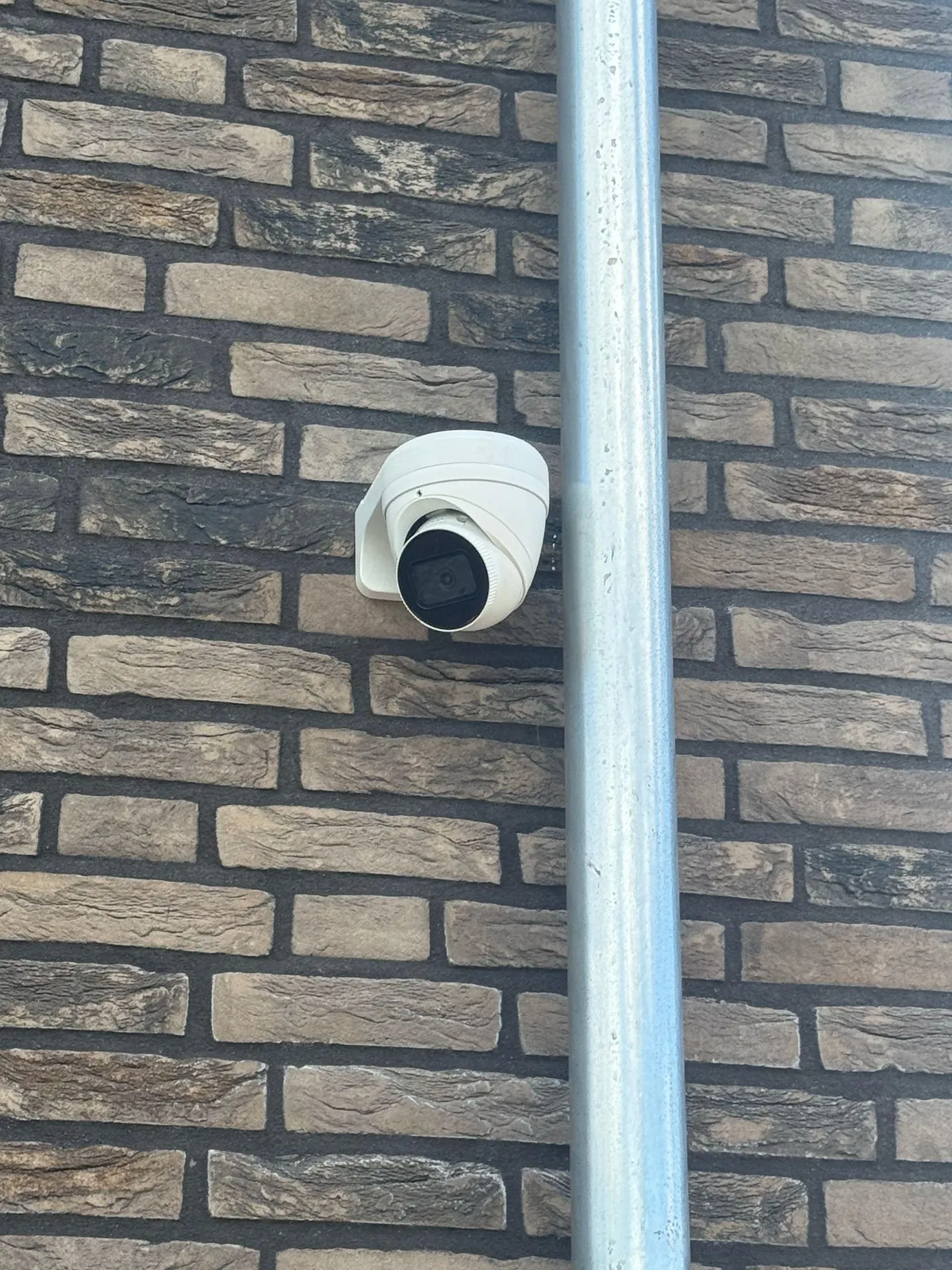 Witte turretcamera op een donkere bakstenen gevel, naast een zilveren regenpijp
