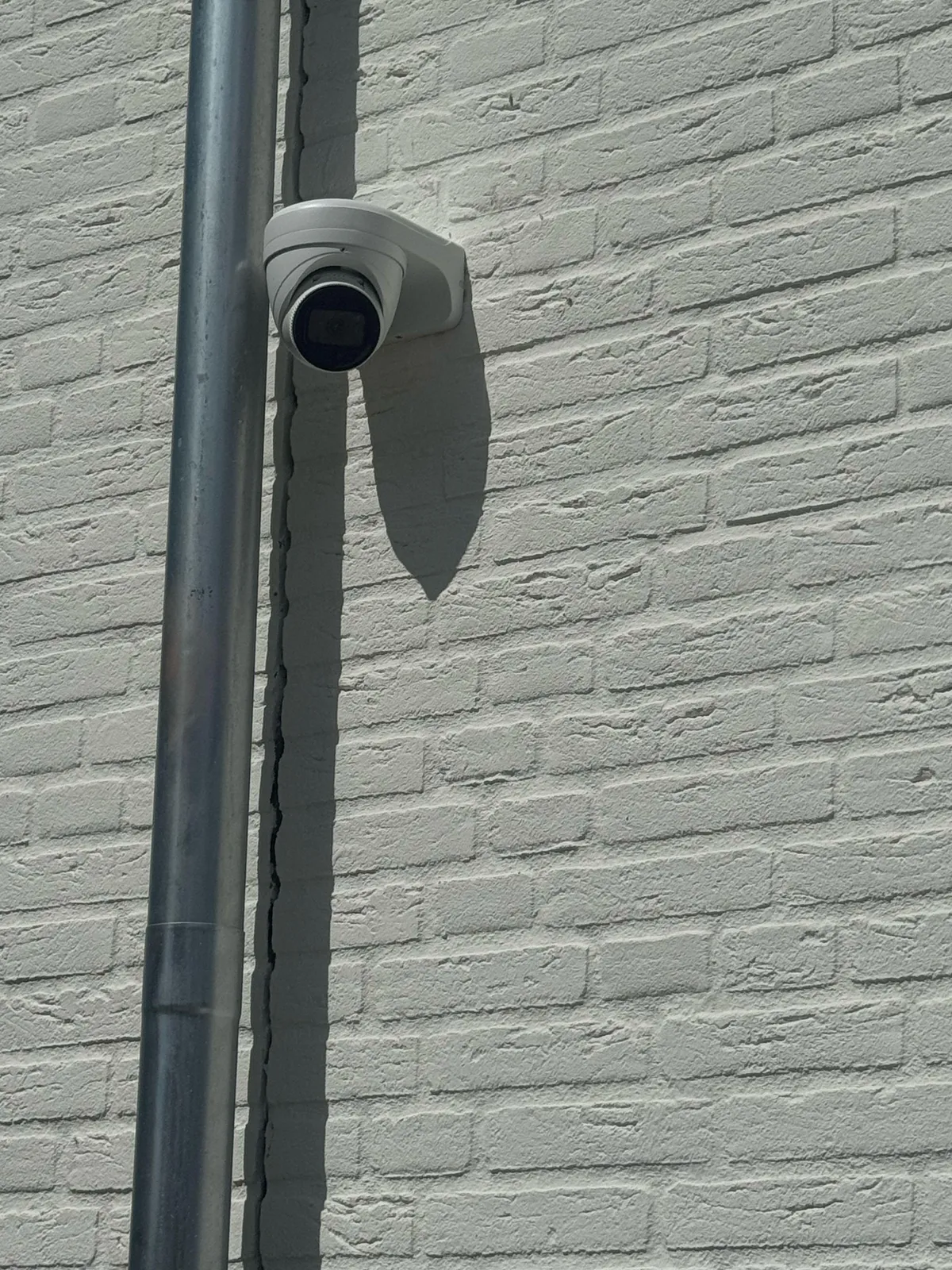 Witte turretcamera op een lichte gevel, direct naast een grijze regenpijp