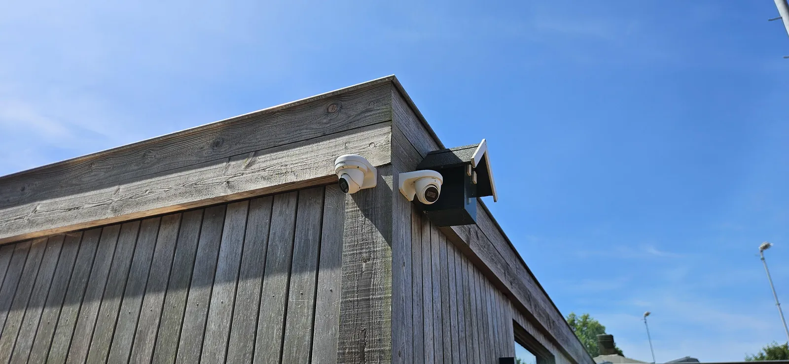 Twee witte turret-camera’s op de hoek van een houten gevel