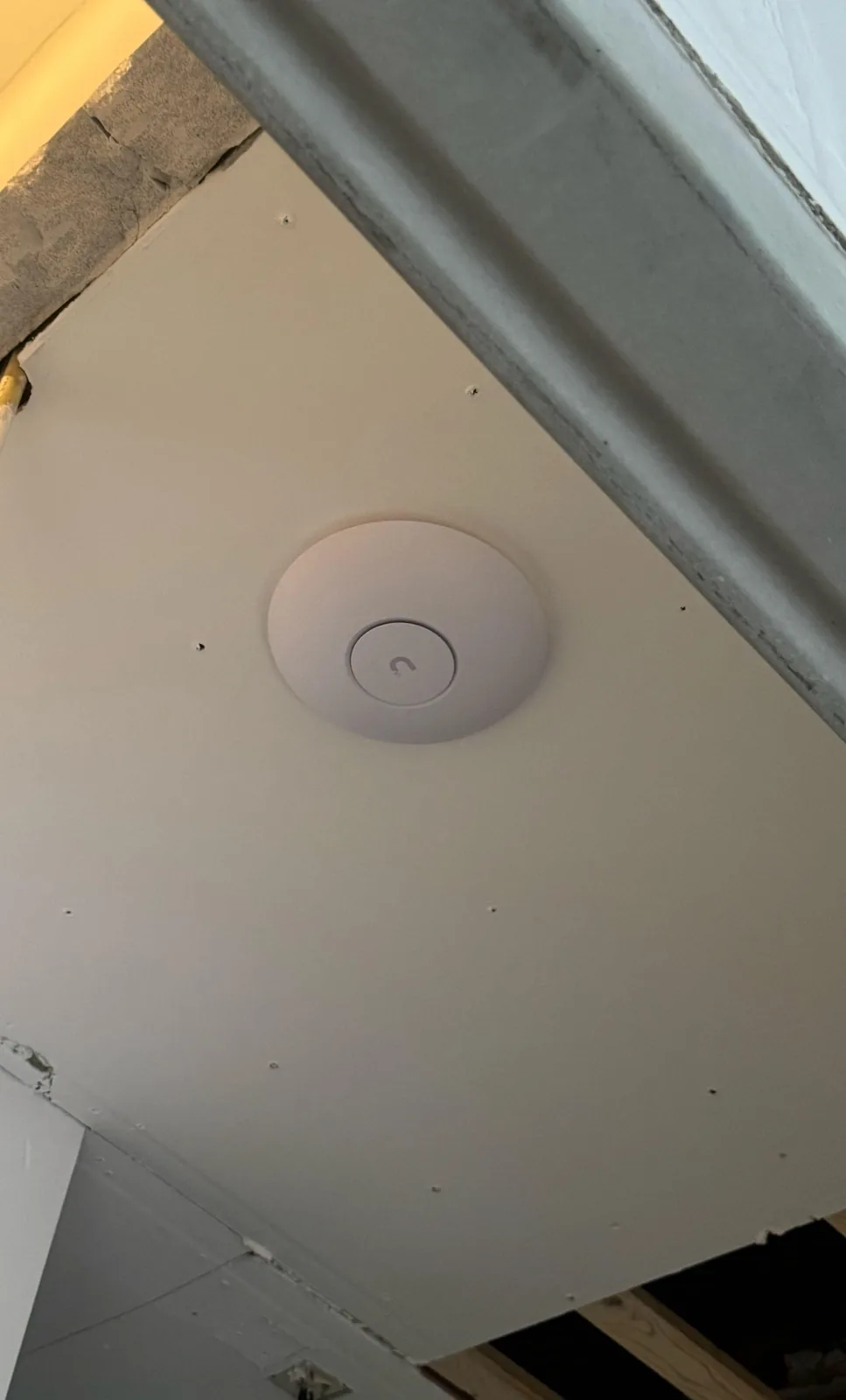 Wit UniFi-access point op een nieuw plafond, terwijl de verbouwing nog bezig is