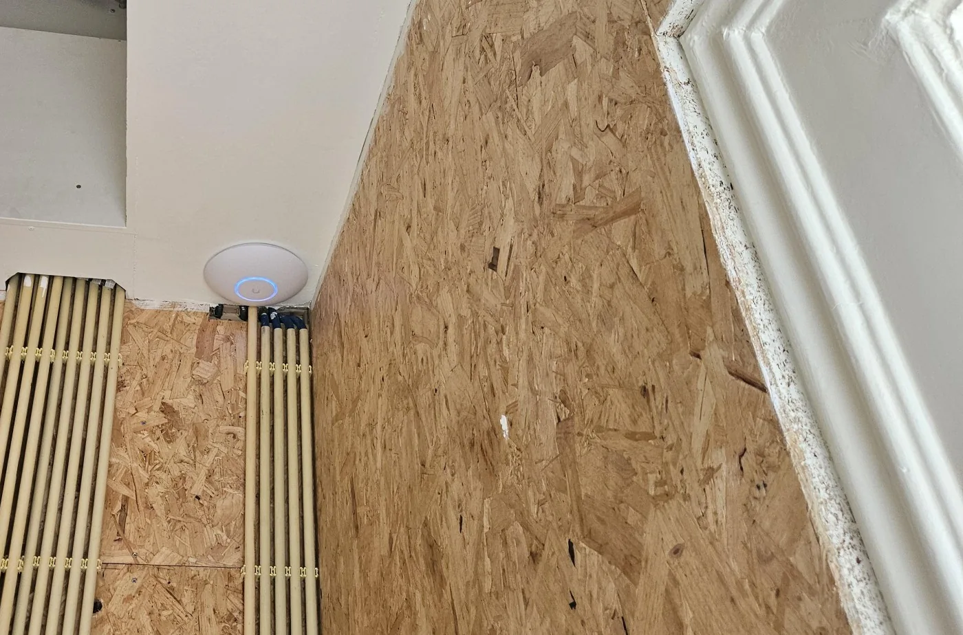 UniFi-accesspoint in de kelder boven twee bundels installatiebuizen langs de wand