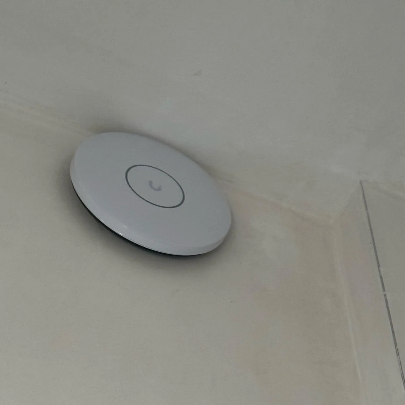 Rond wit UniFi-accesspoint van dichtbij, strak tegen het plafond