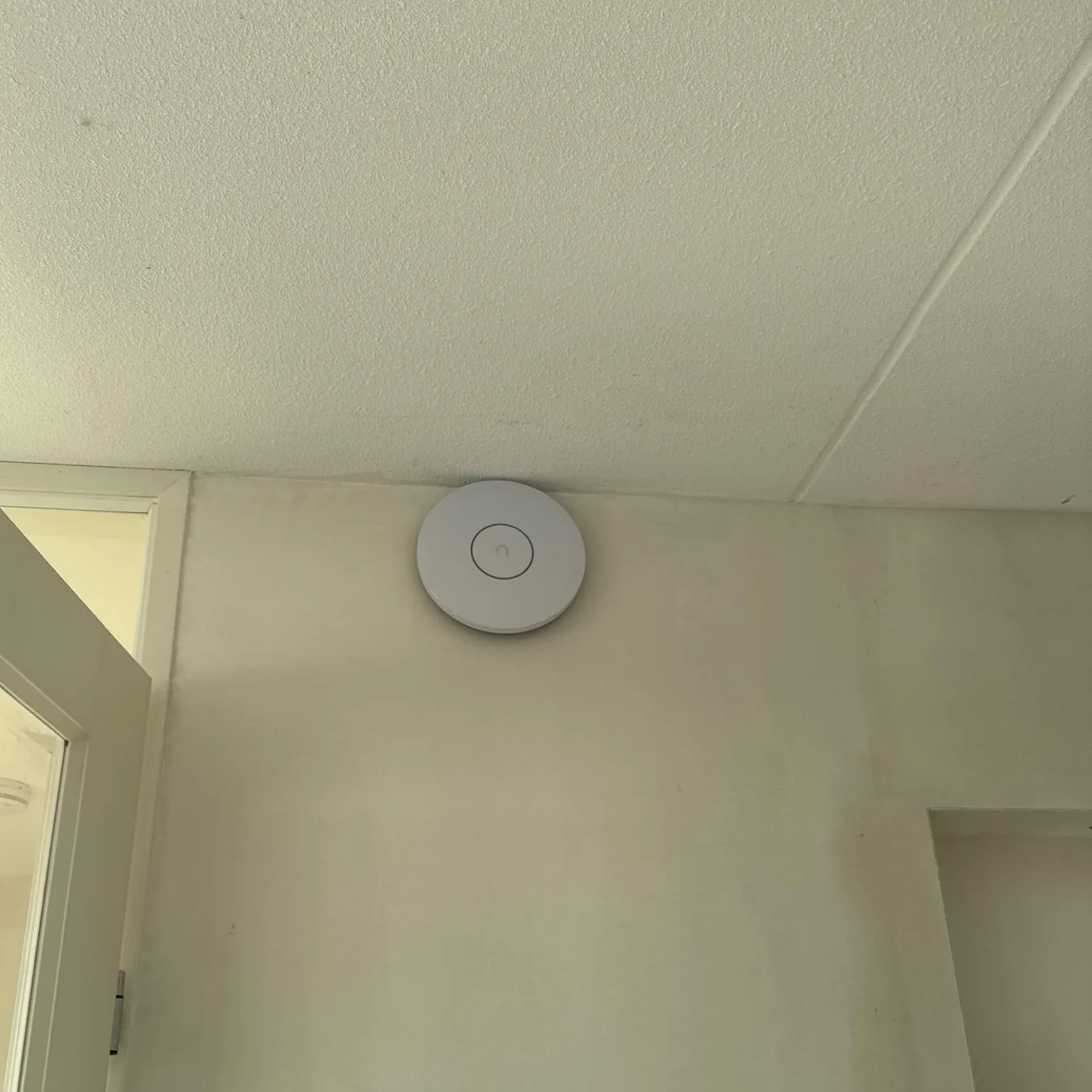 Rond wit UniFi-accesspoint aan het plafond van een lichte hal