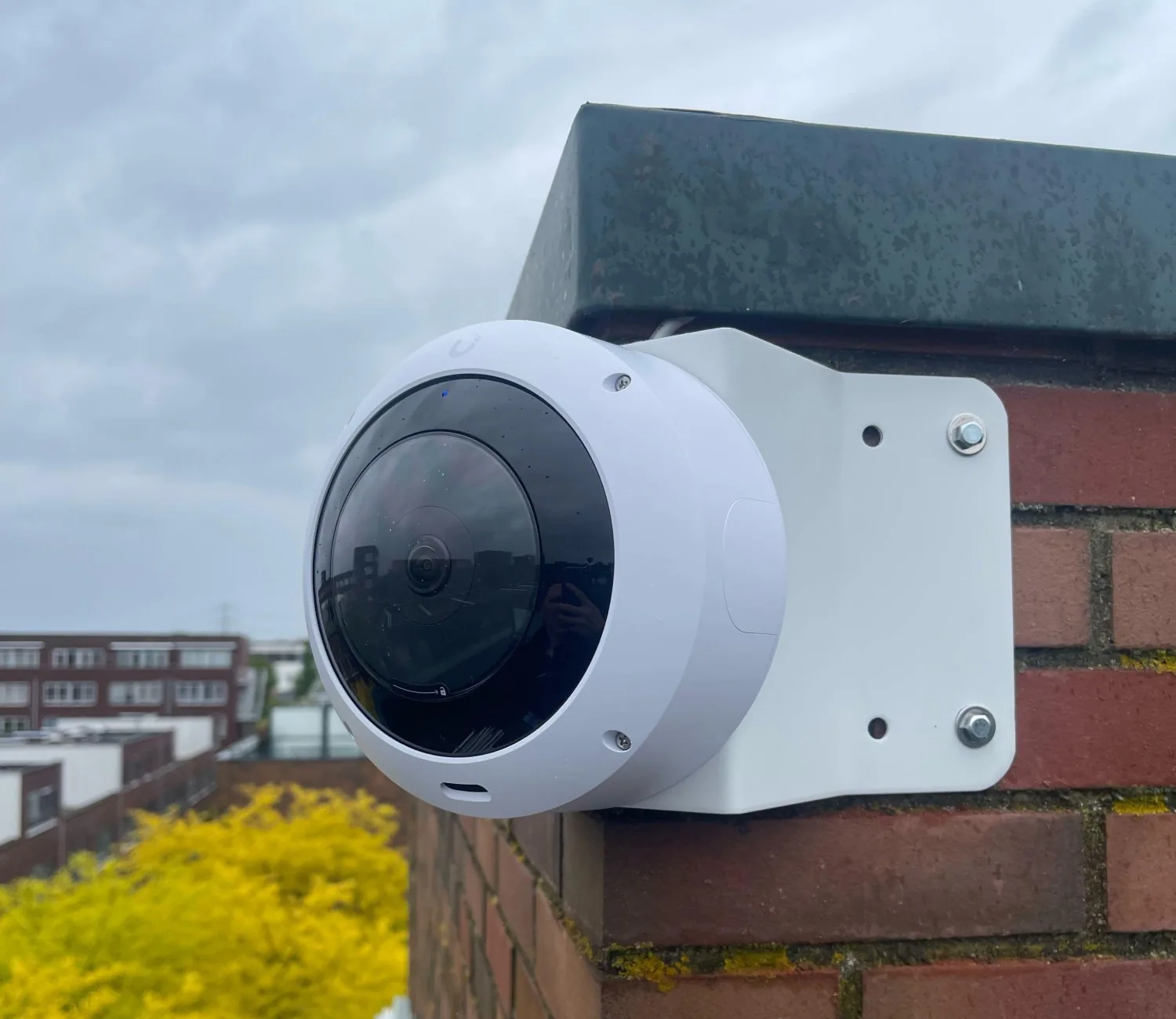 Witte UniFi AI 360-camera op een muurbeugel met hoekbeugel op de rand van een dakterras