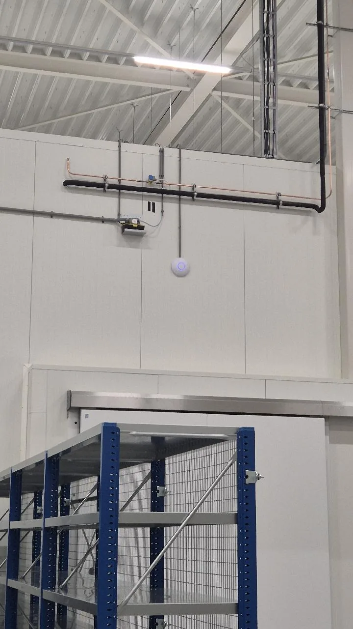 UniFi-access point aan een paneelwand boven een schuifdeur en stellingen