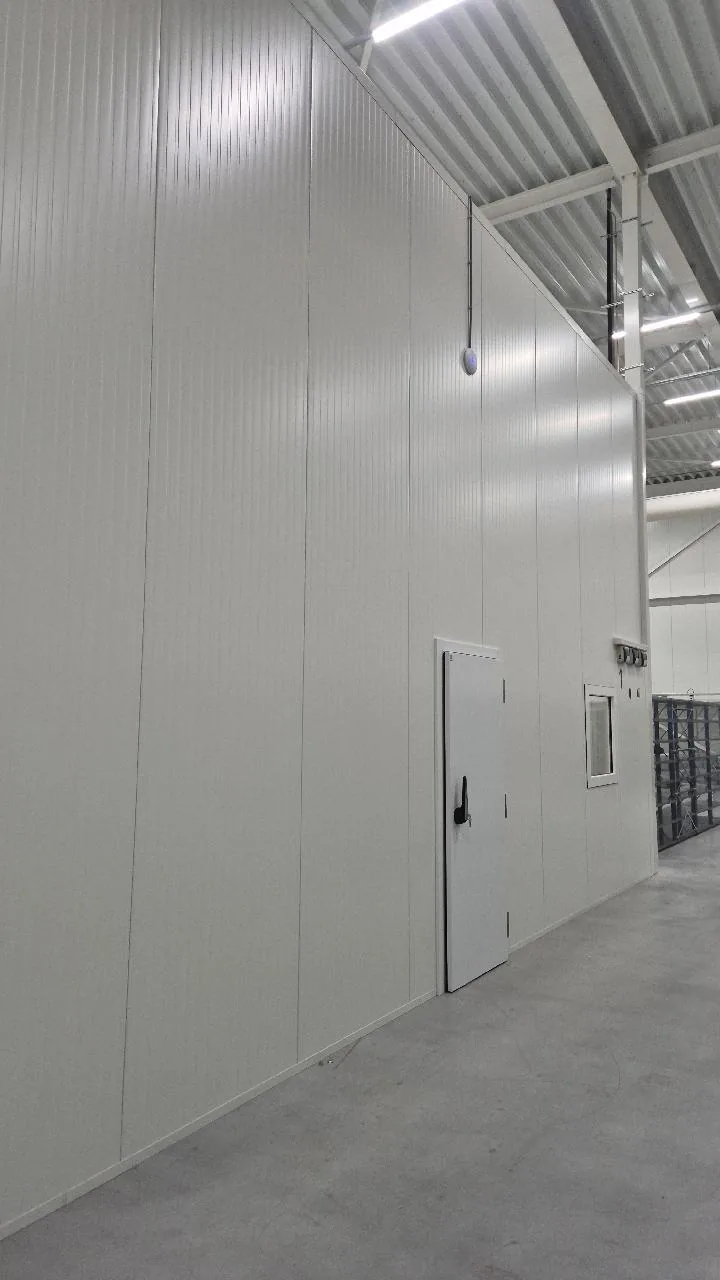 UniFi-access point hoog aan een lange paneelwand in een warehouse, met een deur onderaan