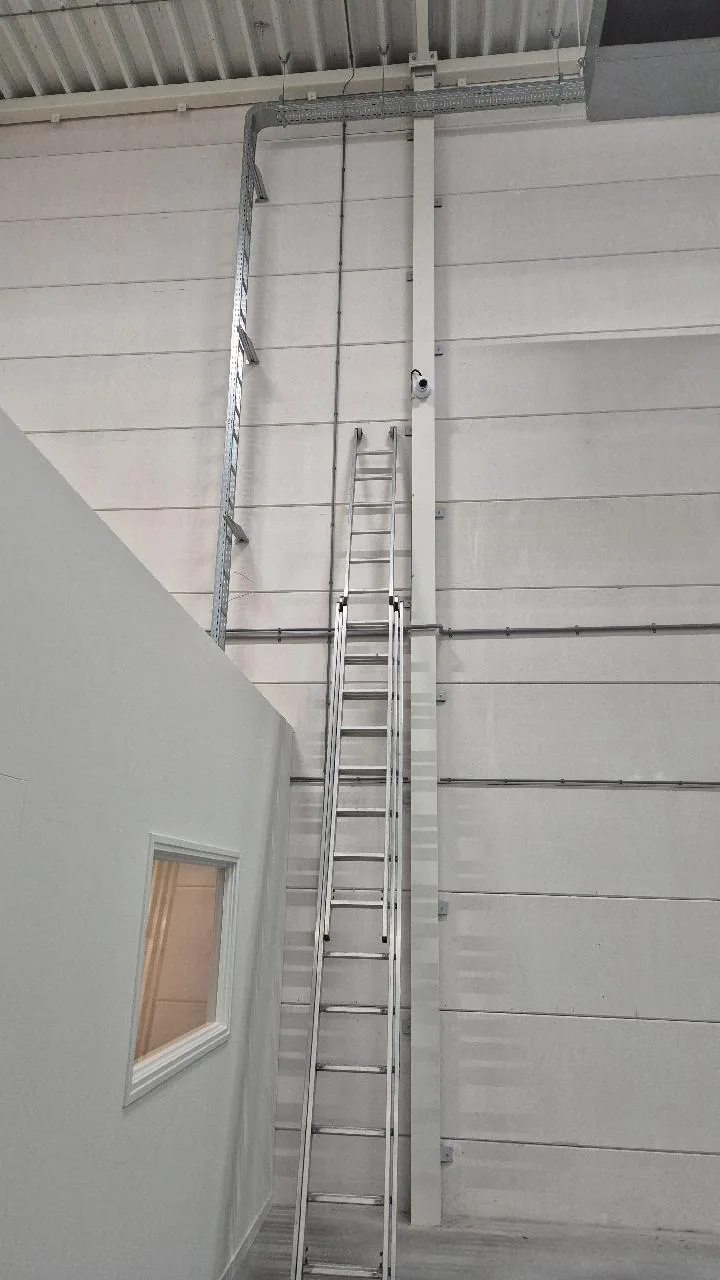 UniFi-camera hoog aan de wand bij een kabelgoot, met een ladder ernaast