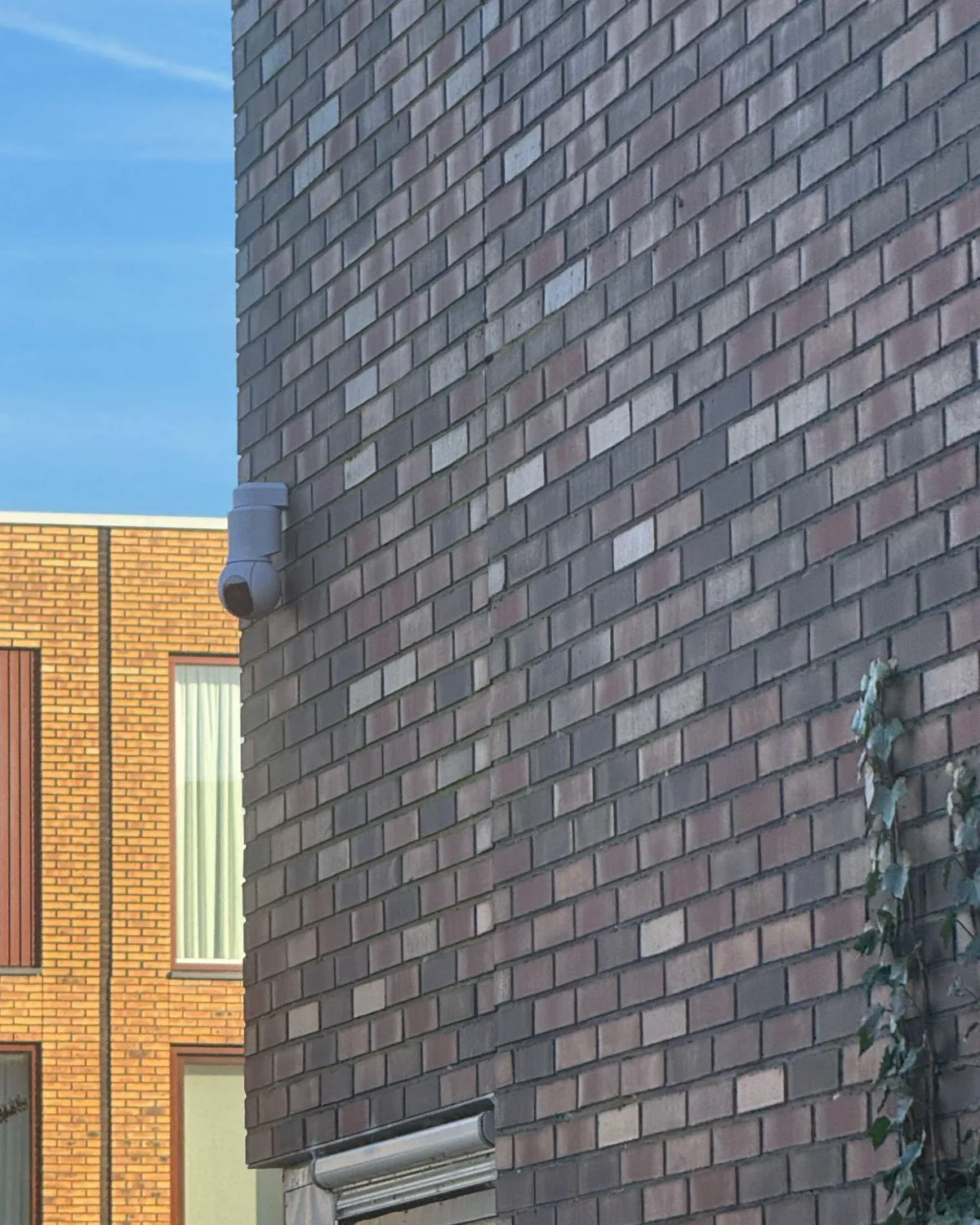 UniFi-camera hoog op een bakstenen zijgevel, met uitzicht langs de gevel