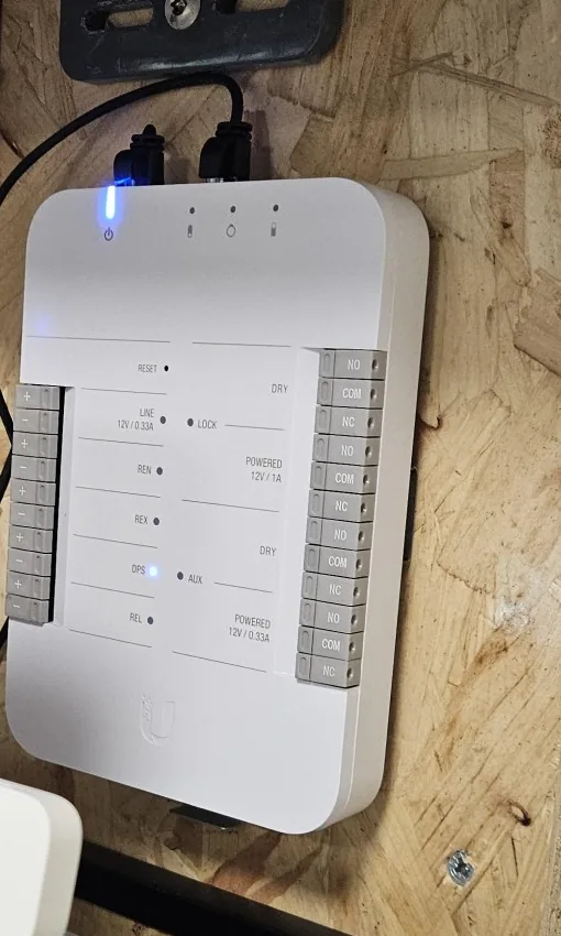 Witte UniFi Door Hub tegen een houten wand boven het patchrek in de kelder