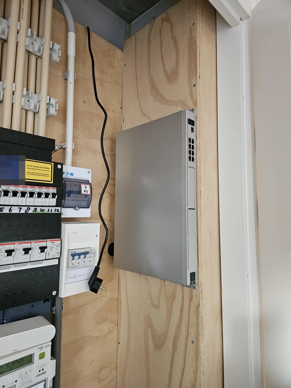 De UniFi Dream Machine rechtop naast de groepenkast, met de stroomkabel netjes langs de wand