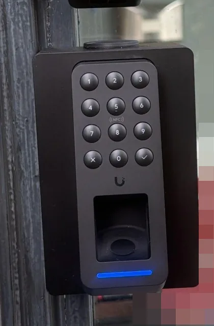 Detail van de zwarte UniFi G3 Reader Fingerprint met cijfertoetsen, NFC en vingerafdrukvenster, op een zwart opbouwkastje aan een donker kozijn