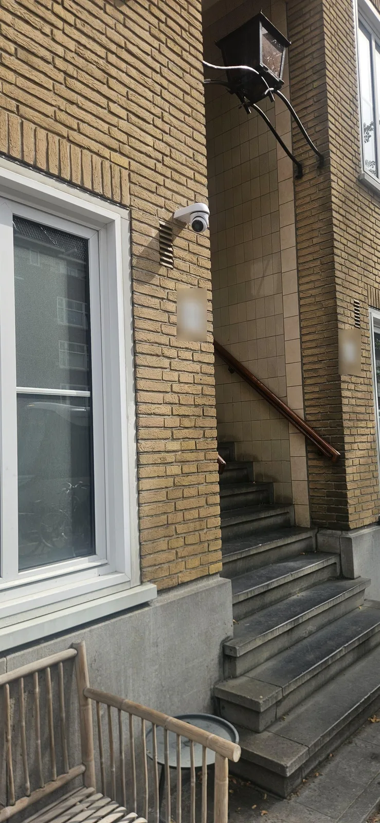 Witte UniFi-camera hoog op de gevel boven de stenen trap van een portiek in Amsterdam